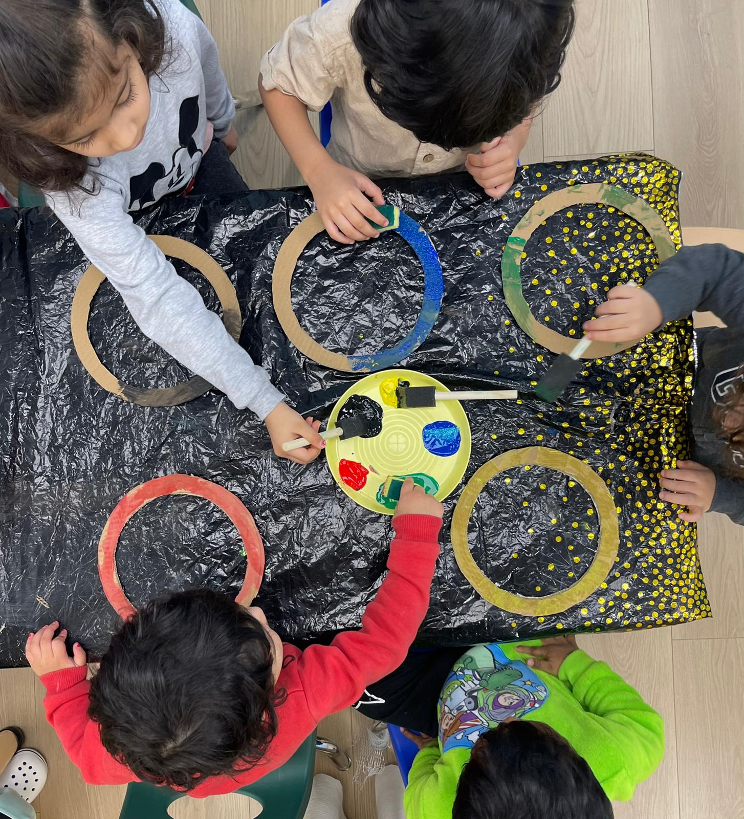 Children work together painting cardboard rings around a tray of paint.