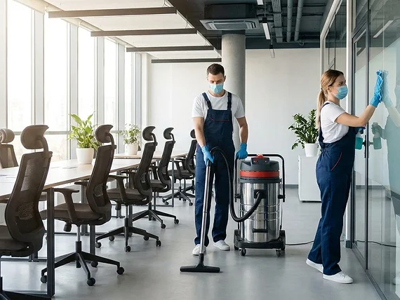 Office cleaner sanitizing desks and surfaces in an open workspace — office cleaning services